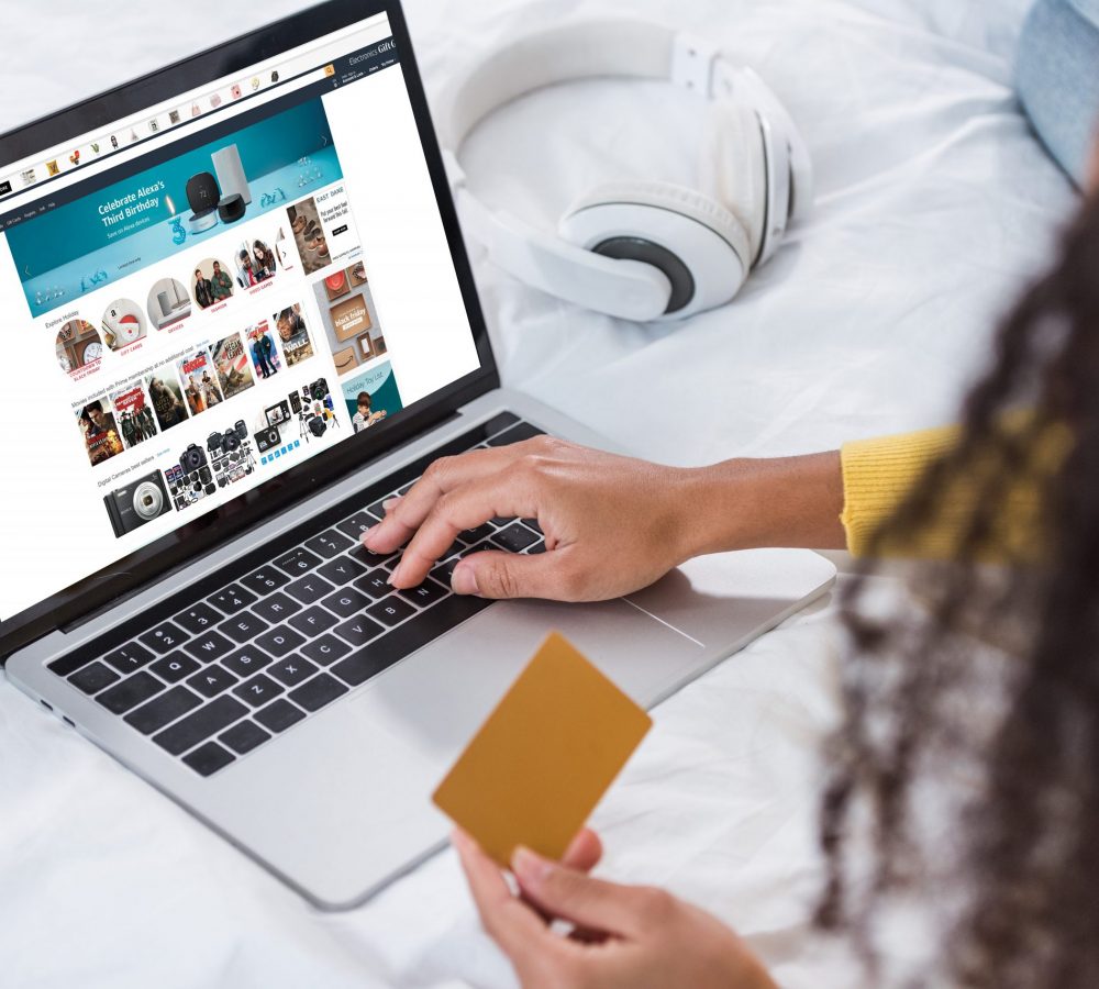 cropped image of woman holding credit card and using laptop with amazon  on screen